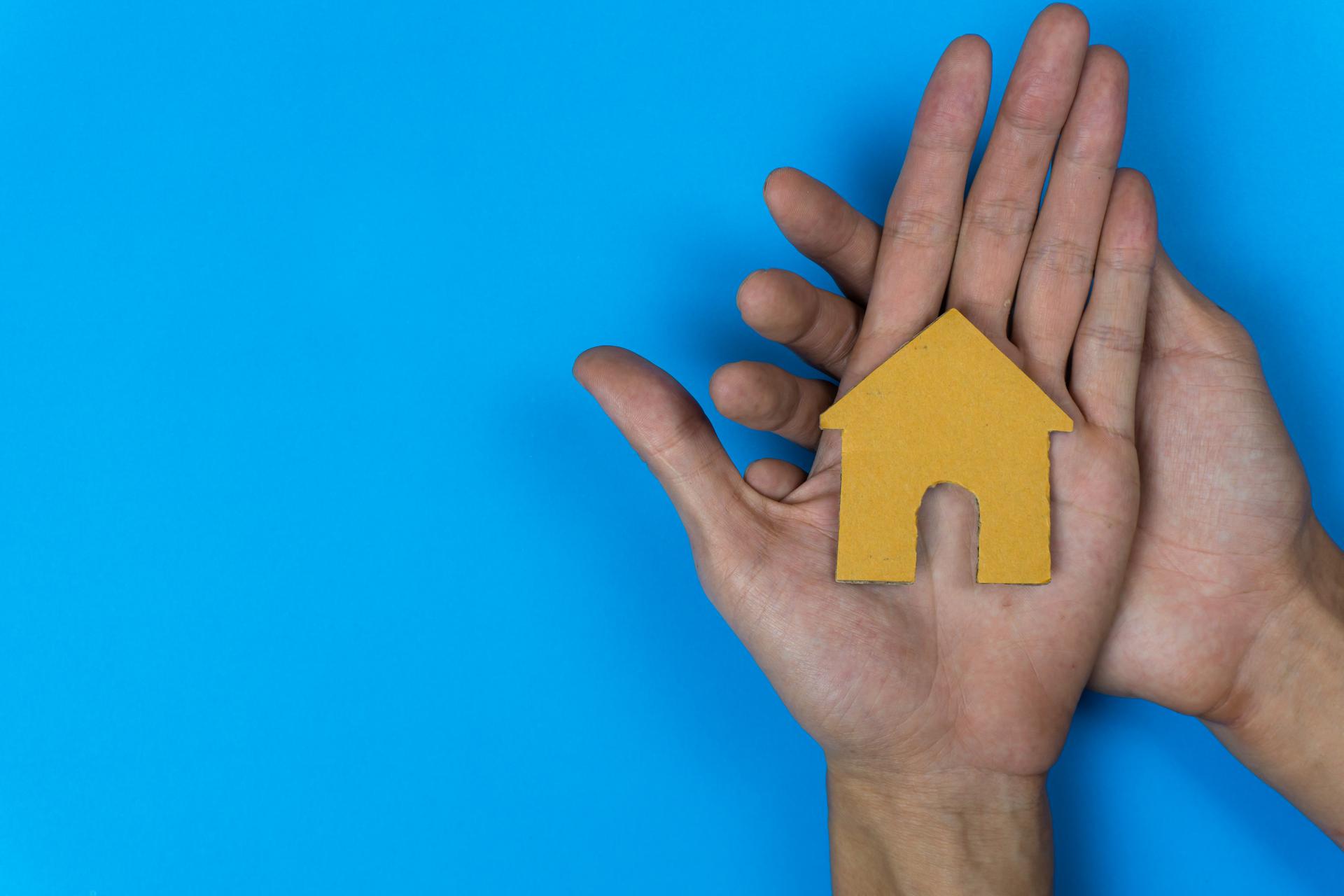 Buy or rent. A small house model made by paper cut on a man hand on  blue background.