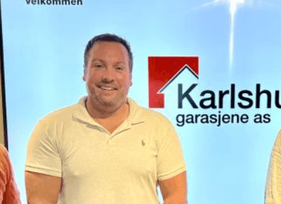 Man in white polo shirt standing in front of a screen with Karlshus logo and text.