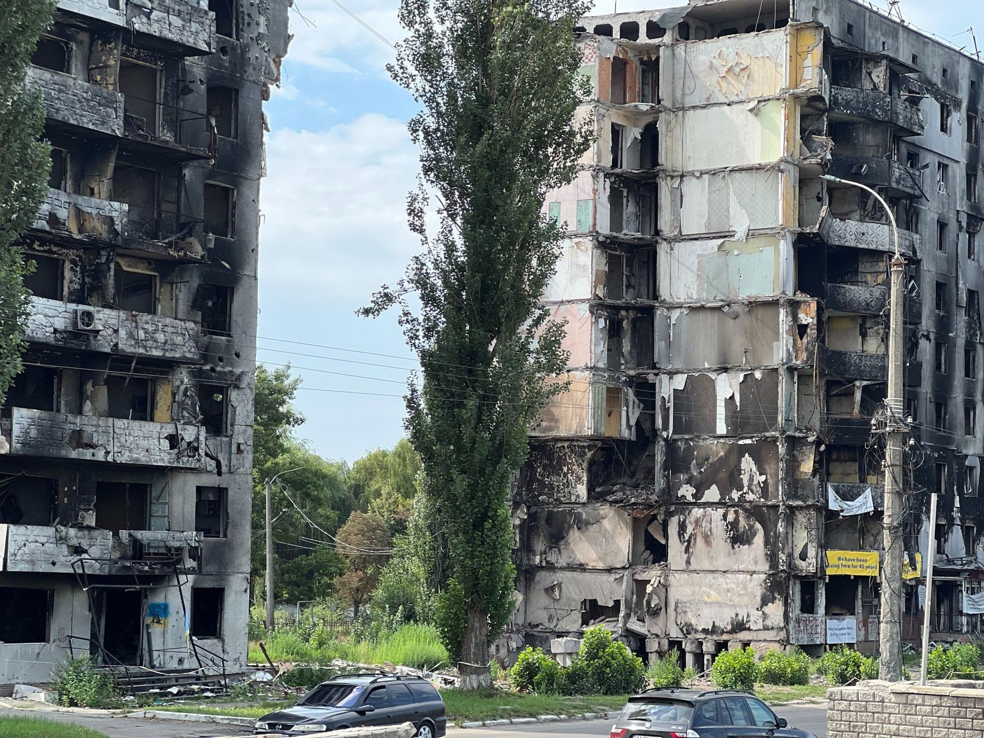 Burned and damaged apartment buildings with visible debris and broken windows surrounded by greenery.